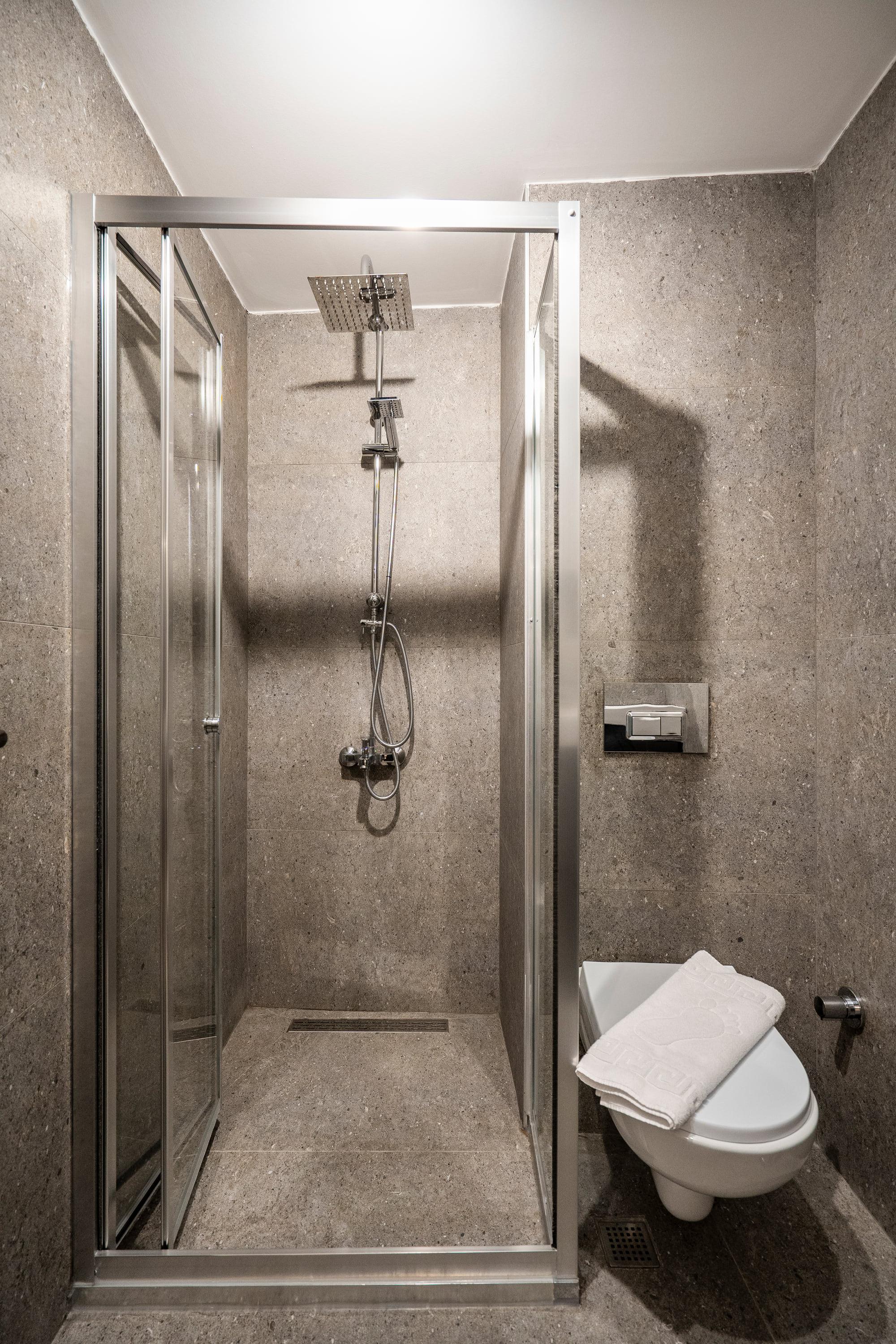 Glass-enclosed shower in the stone-clad bathroom