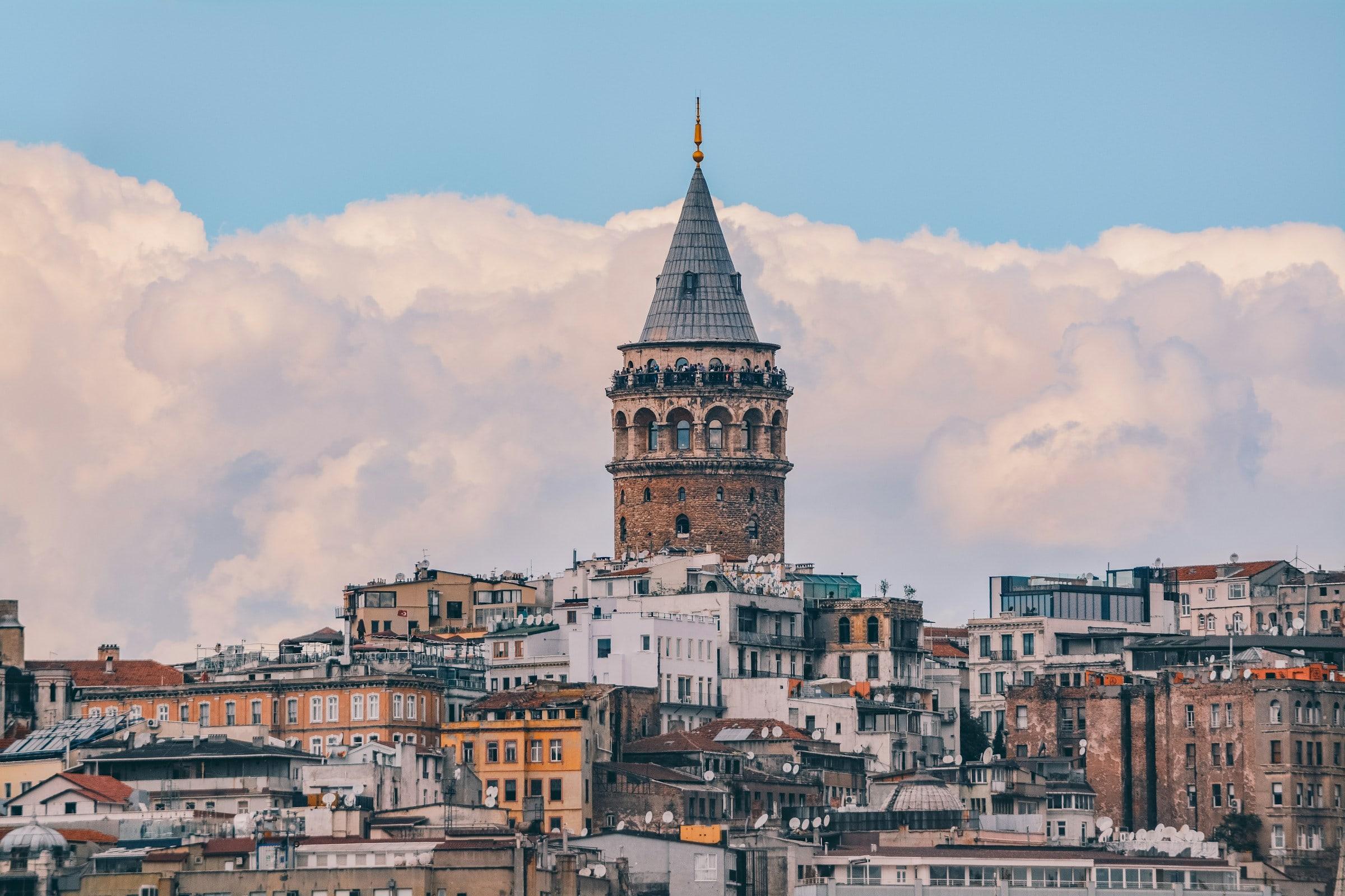 Galata Tower standing above the rooftops, clouds behind it