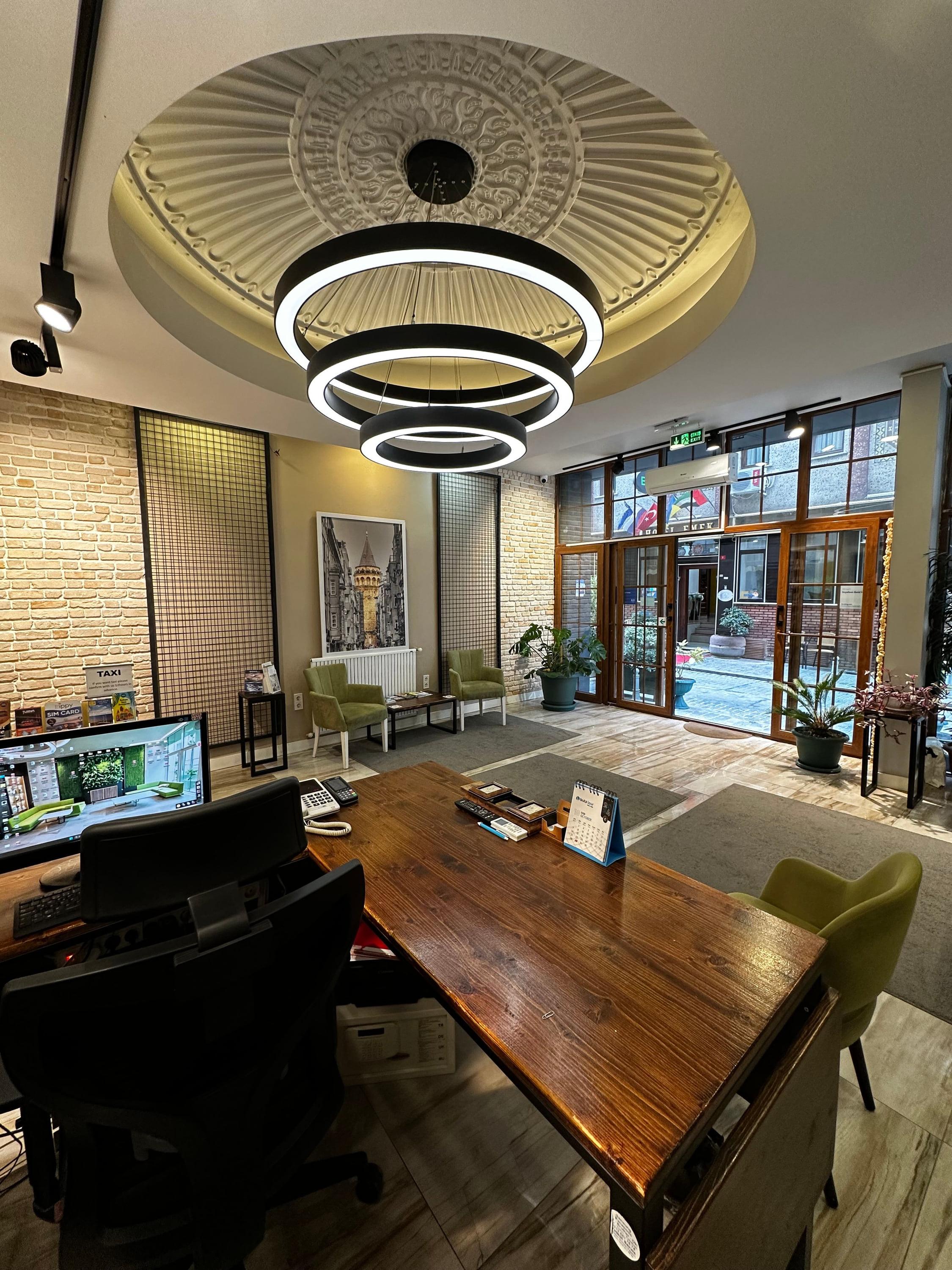 The brick-walled lobby: a wooden reception desk, green armchairs and a ring light under a moulded ceiling