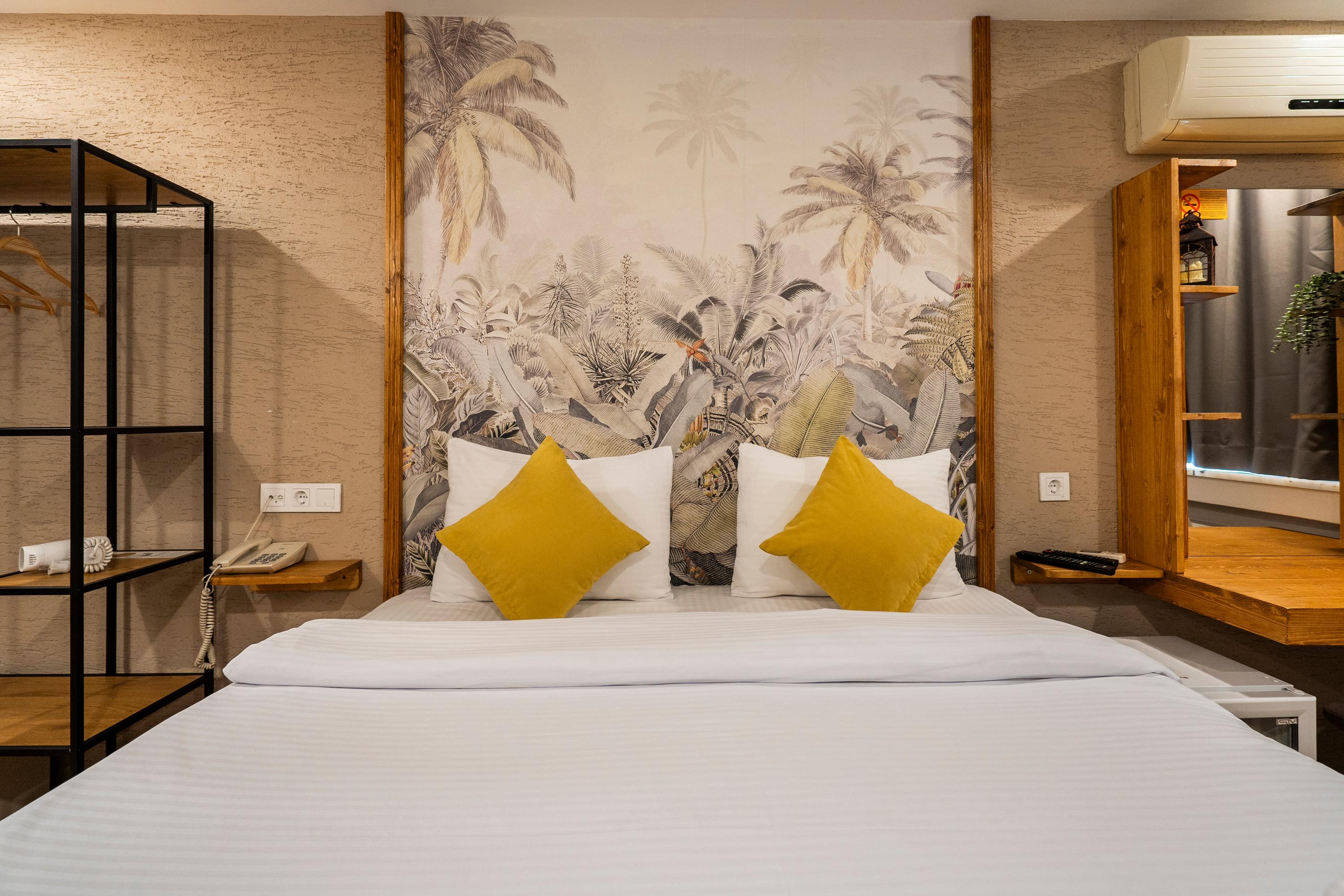 The bed and mustard cushions in front of the botanical mural